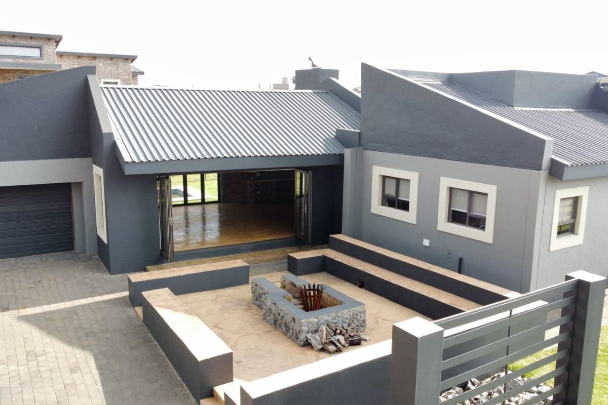 An elevated view of the rear exterior featuring a sunken fire pit area, paved courtyard, and seamless indoor-outdoor flow through large folding doors.