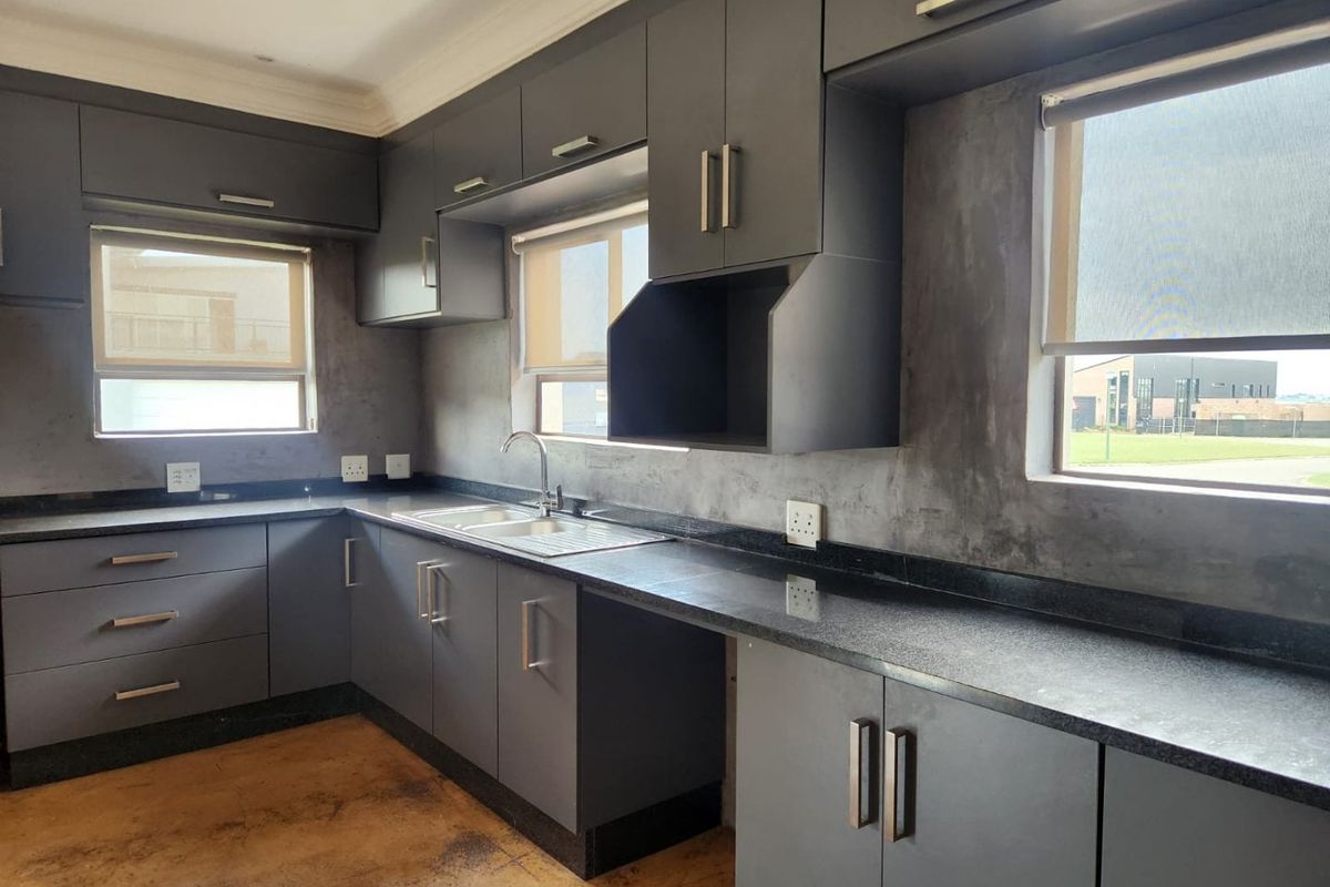 Modern kitchen featuring dark grey cabinetry, granite countertops, stainless steel sink, and polished concrete flooring with large windows for natural light.