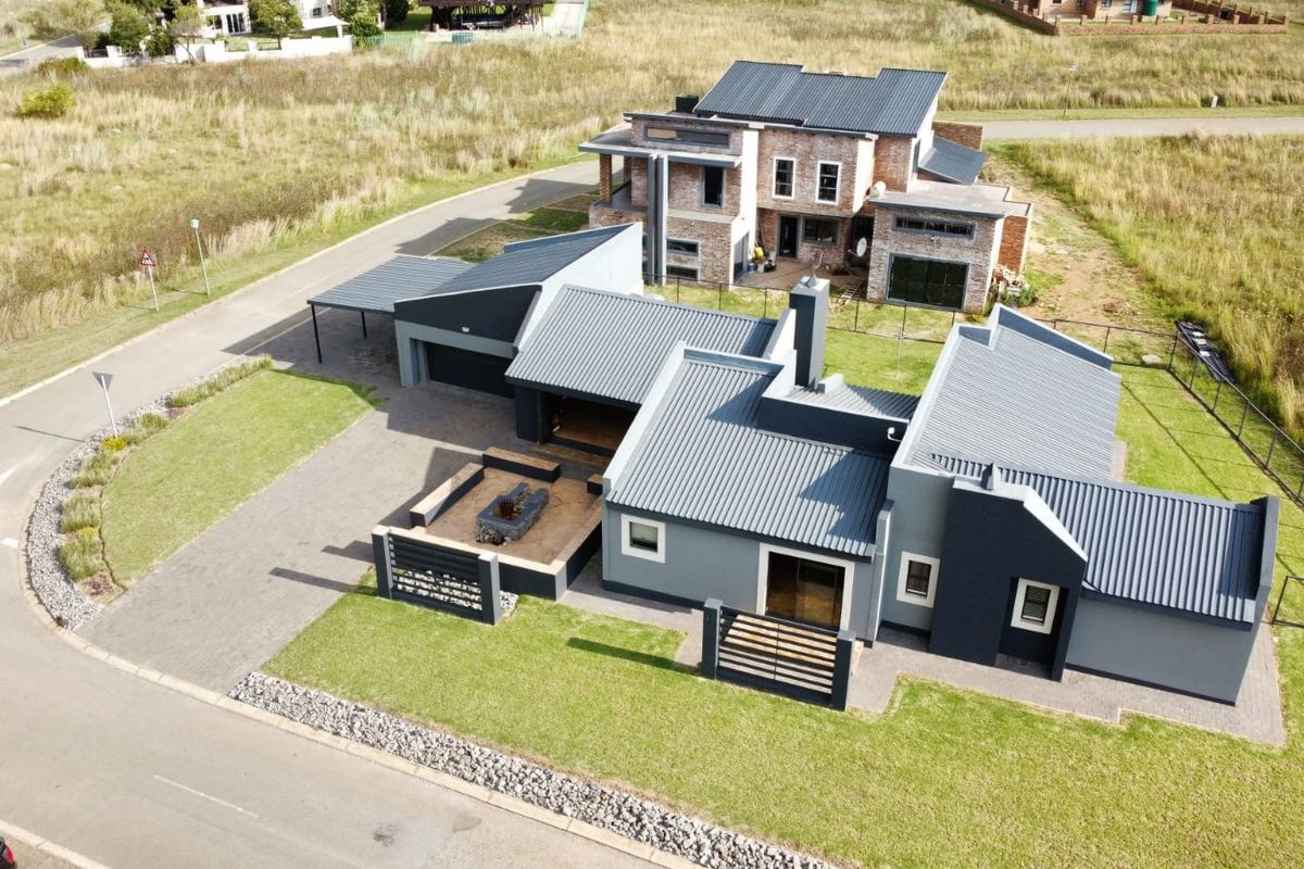 Aerial view of a modern residential property featuring a contemporary architectural design, metal roofing, paved driveway, and an outdoor fire pit area.