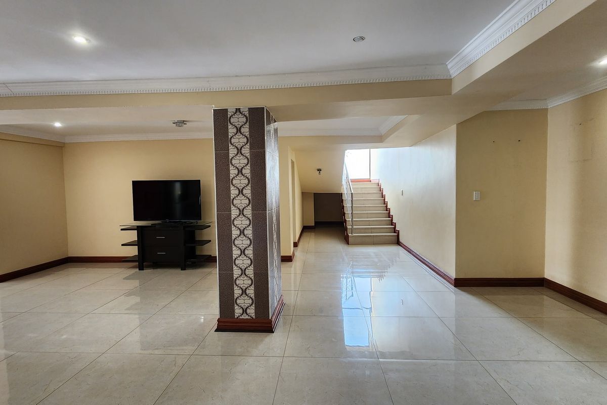 Spacious open-plan living area featuring polished floor tiles, a decorative central column, and a staircase leading to the upper level.
