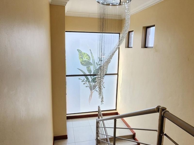 A bright, modern staircase featuring tiled steps, a stainless steel balustrade, and a striking decorative pendant light fixture.