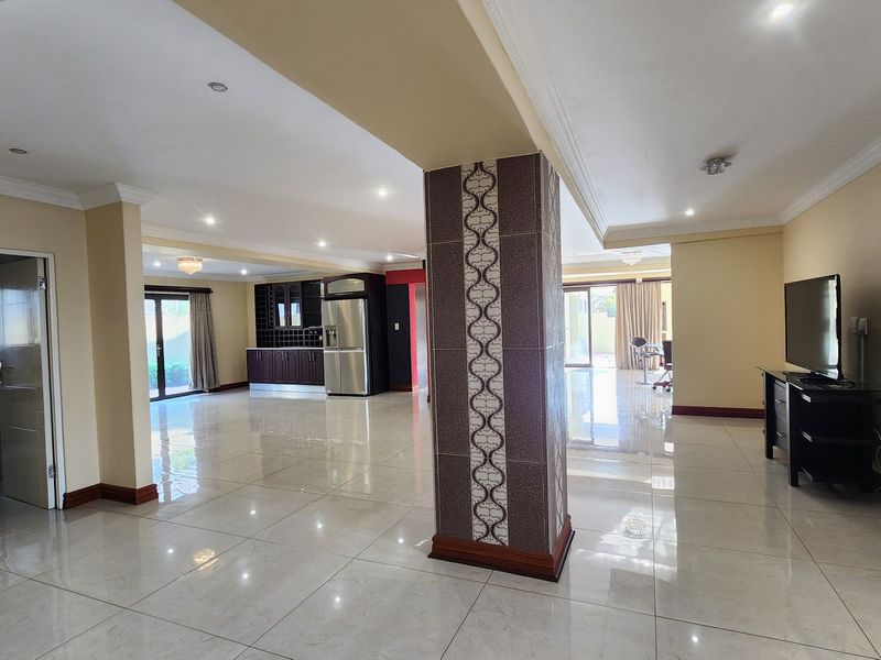 Spacious open-plan living area featuring large format floor tiles, recessed lighting, and a central decorative pillar, seamlessly connecting to the kitchen and outdoor space.