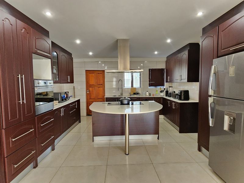 Spacious kitchen featuring dark wood cabinetry, a central island with stone countertop, built-in oven, extractor fan, and tiled flooring.