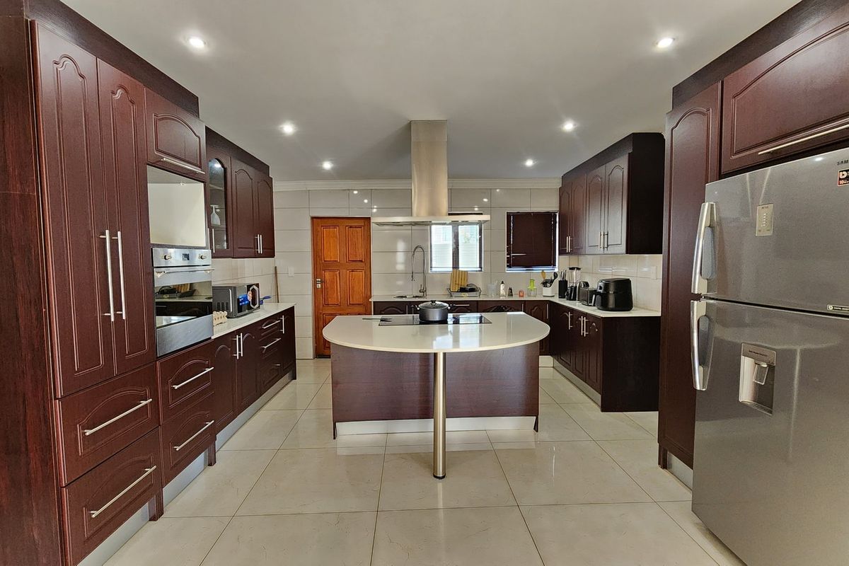 Spacious kitchen featuring dark wood cabinetry, a central island with stone countertop, built-in oven, extractor fan, and tiled flooring.