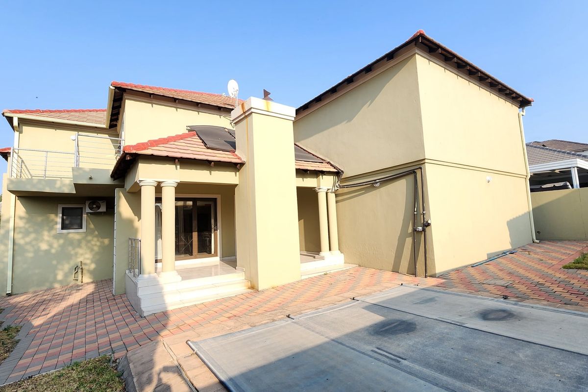 Rear view of a multi-story house featuring a paved patio area, a concrete pool cover, and a balcony with metal railings.