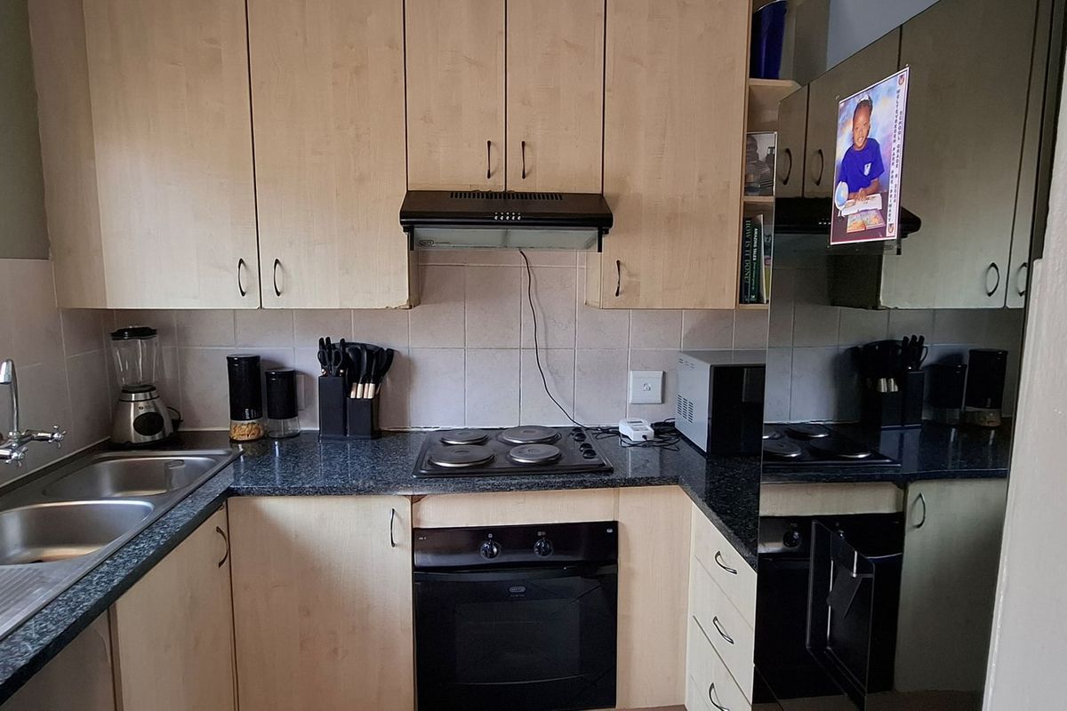 A functional kitchen featuring light wood-tone cabinetry, granite countertops, a built-in oven with hob, and a double stainless steel sink with tiled backsplash.