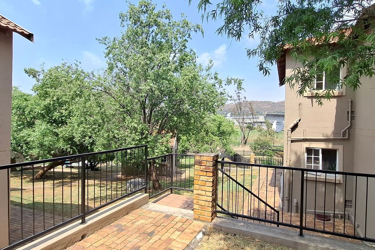 Rear exterior view of the apartment complex featuring a paved patio area, metal balustrades, and established garden surroundings.