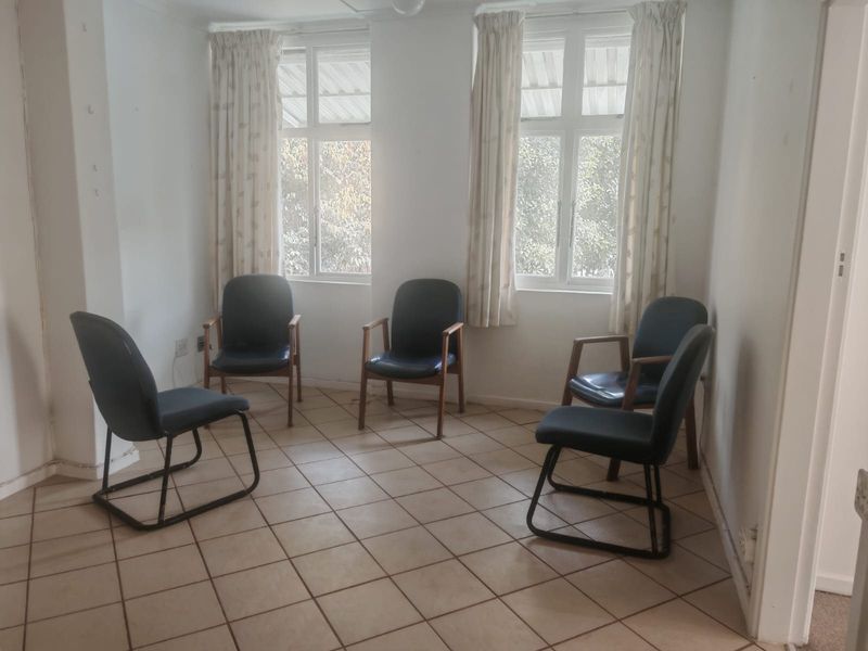 A living area featuring tiled flooring and dual casement windows, currently used as a seating space with dated wall finishes.