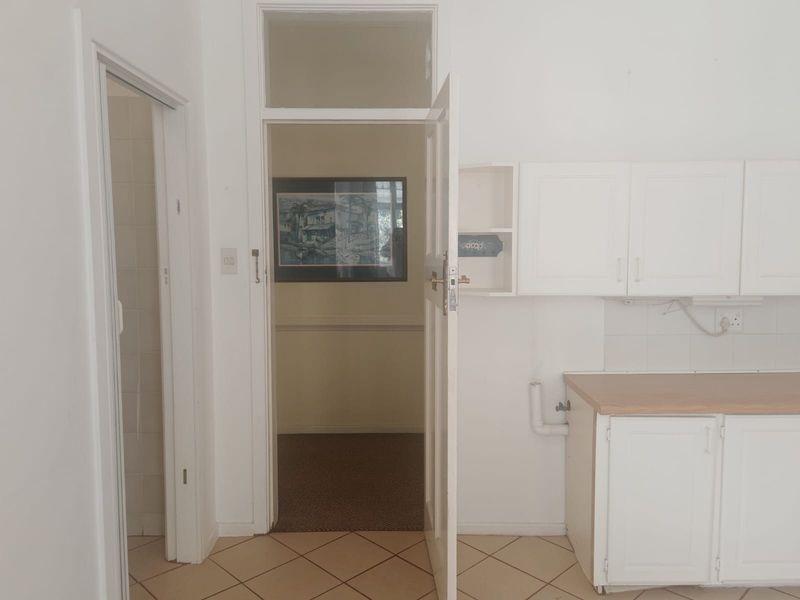 A functional kitchen area featuring white built-in cabinetry, laminate countertops, and tiled flooring, leading into an adjacent room through a doorway.