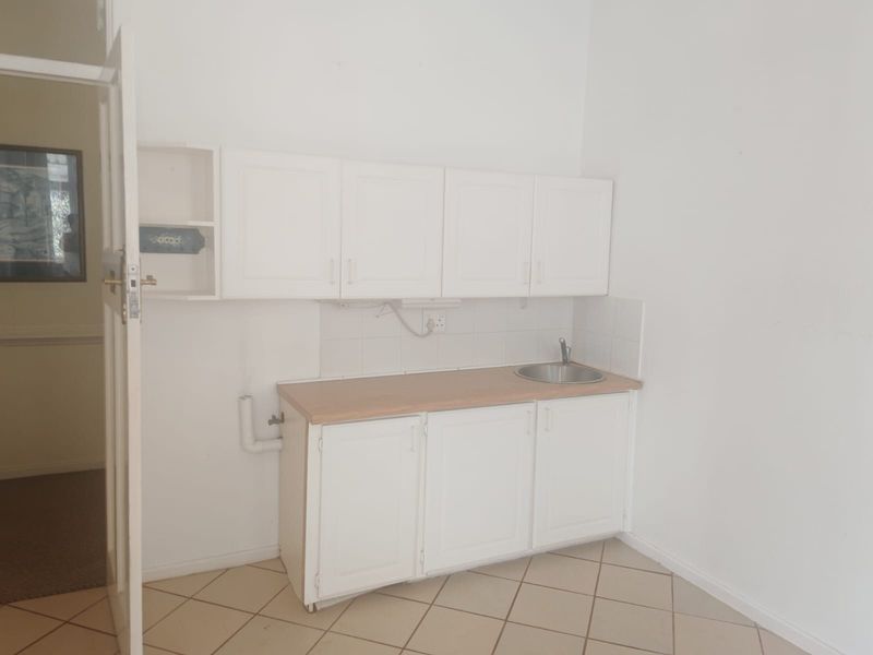 A compact kitchen area featuring white built-in cabinetry, a laminate countertop with an integrated sink, and tiled flooring.