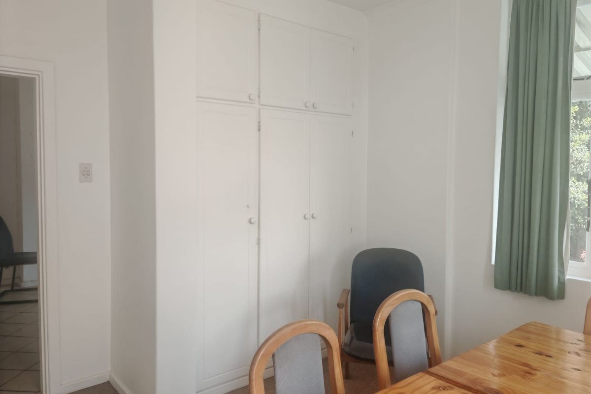A bedroom featuring white built-in cupboards and neutral carpeting, offering a functional space with natural light.