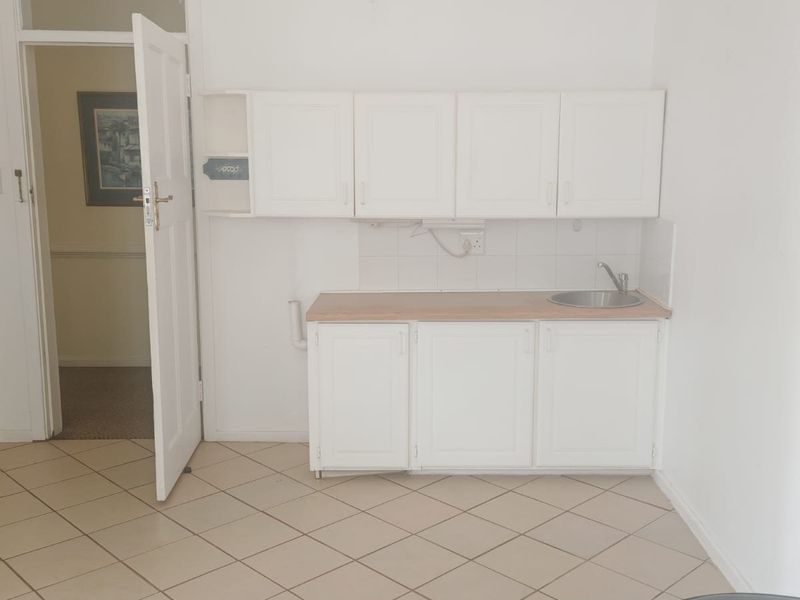 A compact, empty kitchen area featuring white cabinetry, a laminate countertop, a stainless steel sink, and tiled flooring.