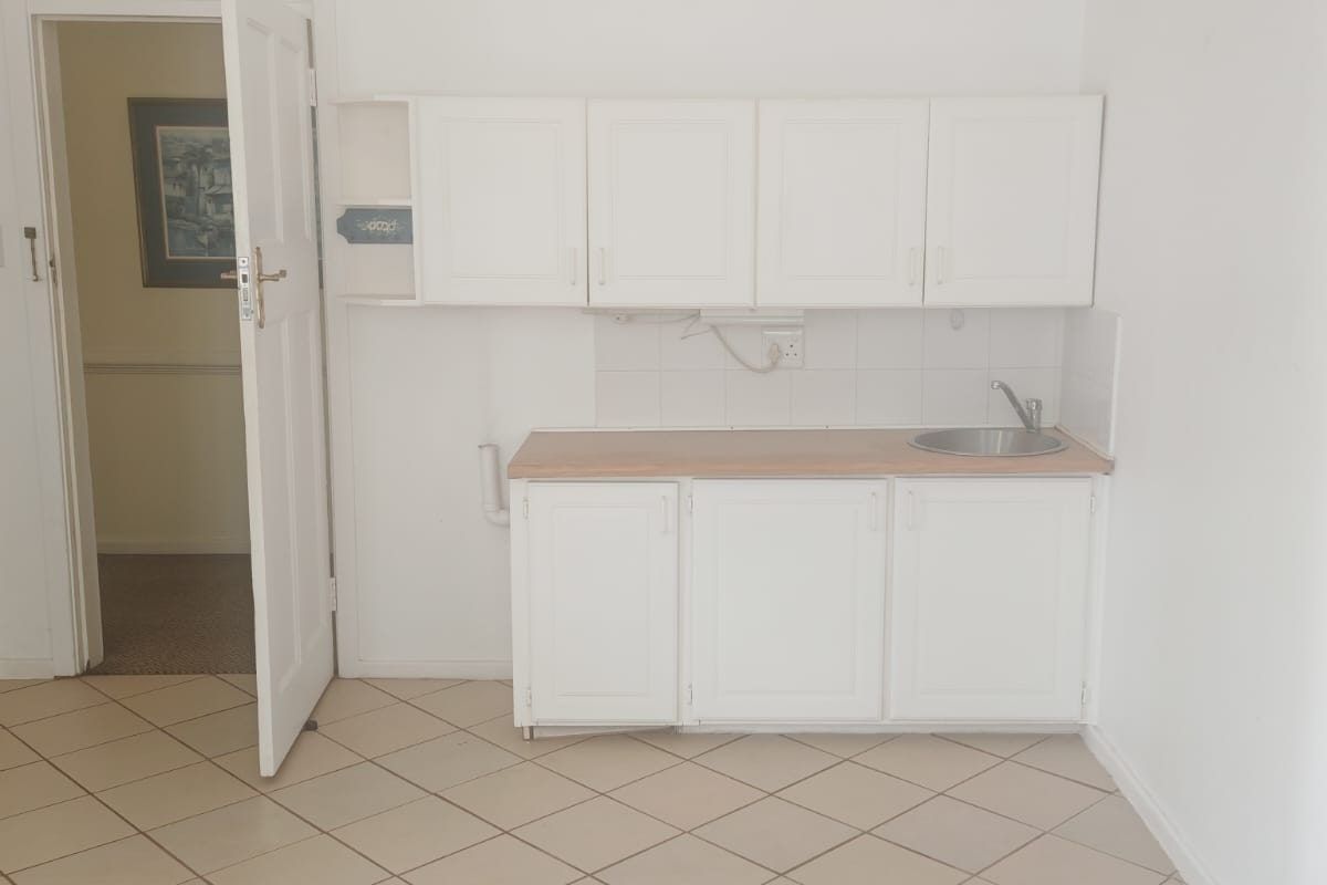 A compact, empty kitchen area featuring white cabinetry, a laminate countertop, a stainless steel sink, and tiled flooring.