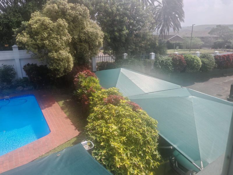 An elevated view of a residential swimming pool area featuring brick paving and a large green shade cloth carport structure.