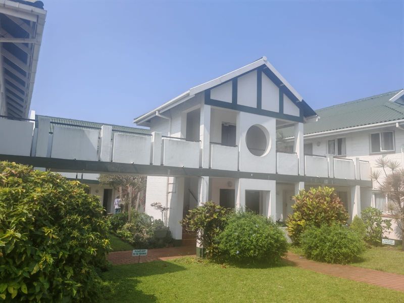 Exterior view of an apartment complex featuring a raised walkway connecting units, surrounded by landscaped gardens and paved pathways.
