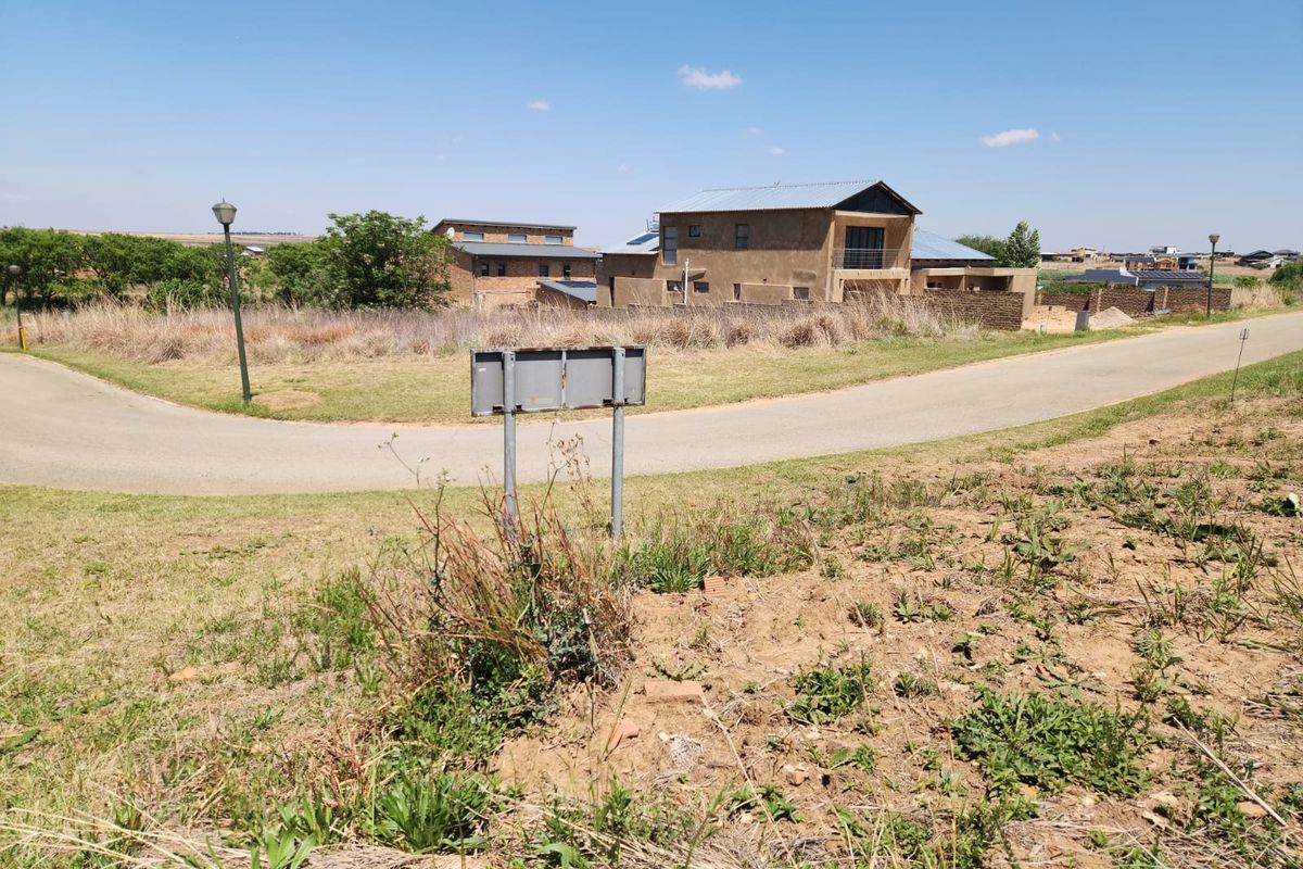 A view of a vacant residential plot situated on a corner, featuring surrounding neighborhood infrastructure and established landscaping.