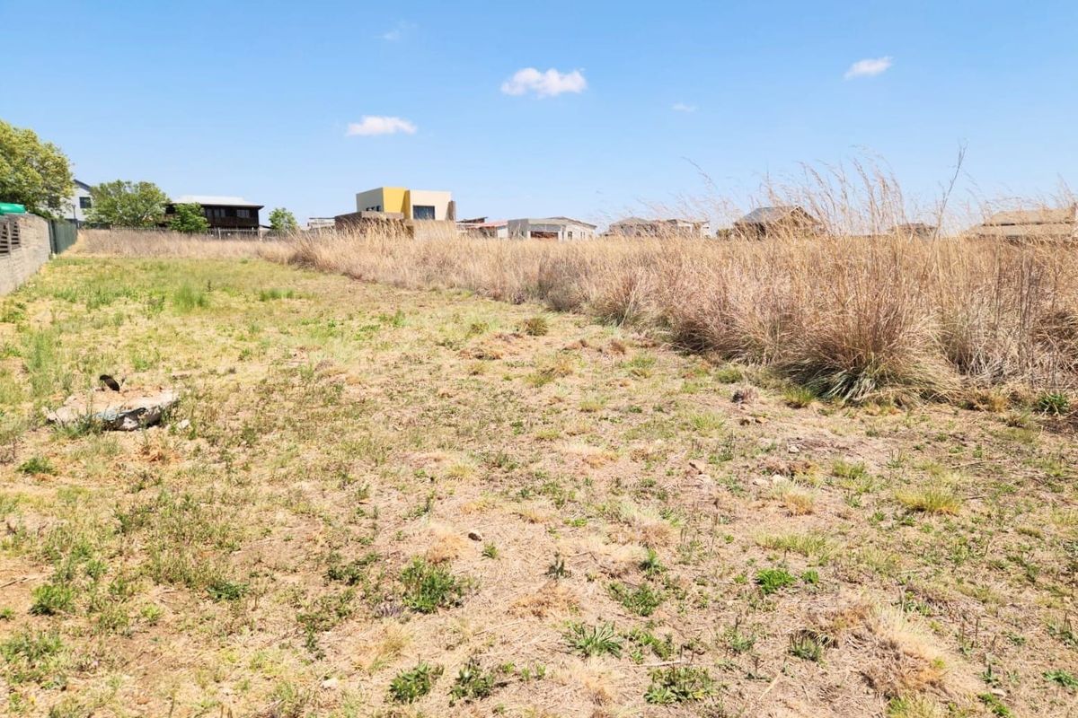A vacant residential plot featuring natural grass and scrub vegetation with established boundary walling in a developed neighborhood setting.