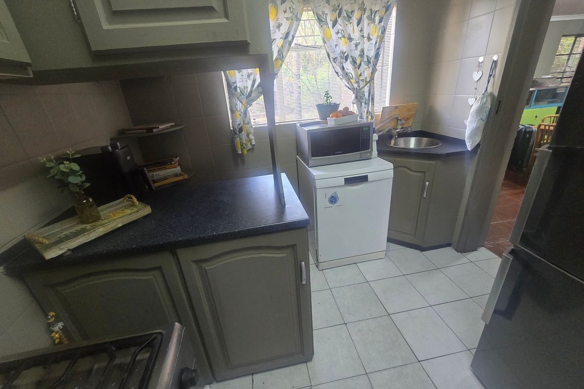 A functional kitchen featuring dark laminate countertops, built-in cabinetry, a stainless steel sink, and tiled flooring.
