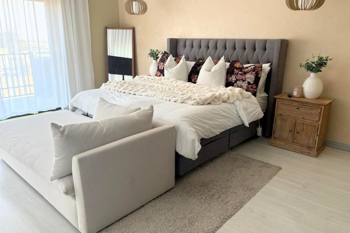 A well-maintained bedroom featuring light laminate flooring, neutral walls, and a sliding glass door providing access to an outdoor balcony area.