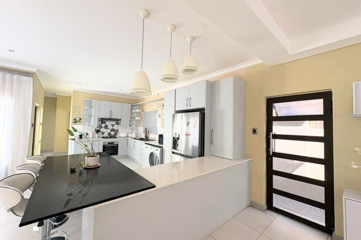 Modern kitchen featuring light grey cabinetry, stone countertops, a breakfast bar, and integrated appliances, with direct access to an exterior door.