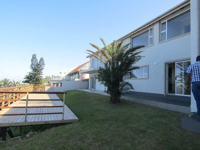 Rear view of the property featuring a timber deck, landscaped lawn, and large sliding glass doors leading into the home.