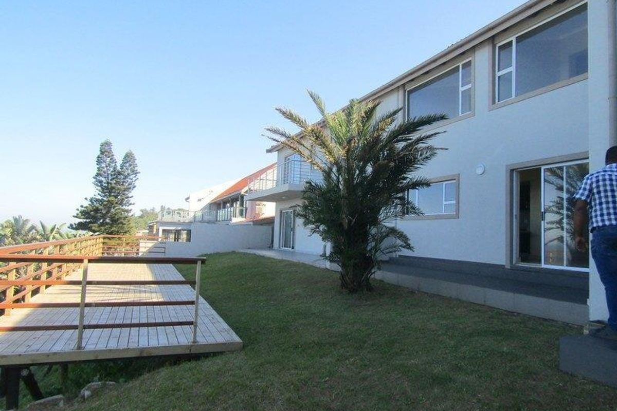 Rear view of the property featuring a timber deck, landscaped lawn, and large sliding glass doors leading into the home.