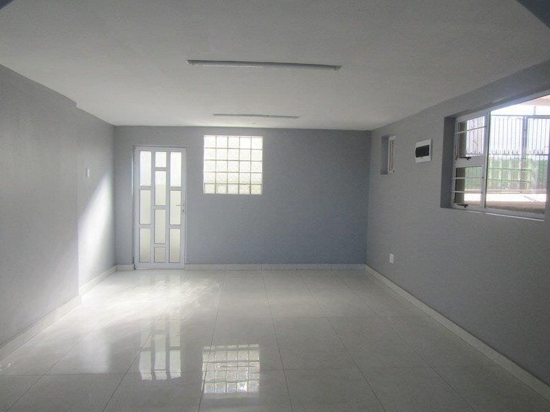 A spacious, empty living area featuring neutral grey walls, polished tiled flooring, a glass block window, and secure access points.