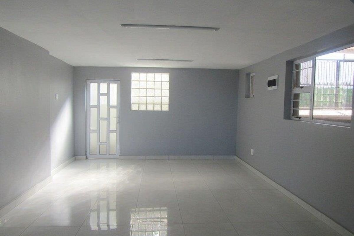 A spacious, empty living area featuring neutral grey walls, polished tiled flooring, a glass block window, and secure access points.
