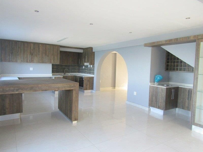 Spacious kitchen featuring modern wood-finish cabinetry, a central island, tiled flooring, and a distinctive architectural archway leading to adjacent living areas.