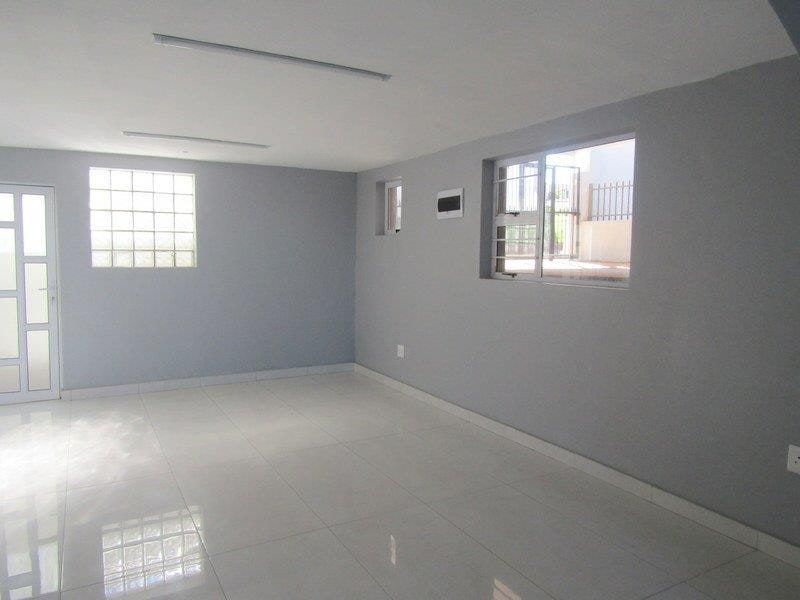 A bright, empty living area featuring neutral grey walls, polished tiled flooring, and natural light from a glass block window and standard window.