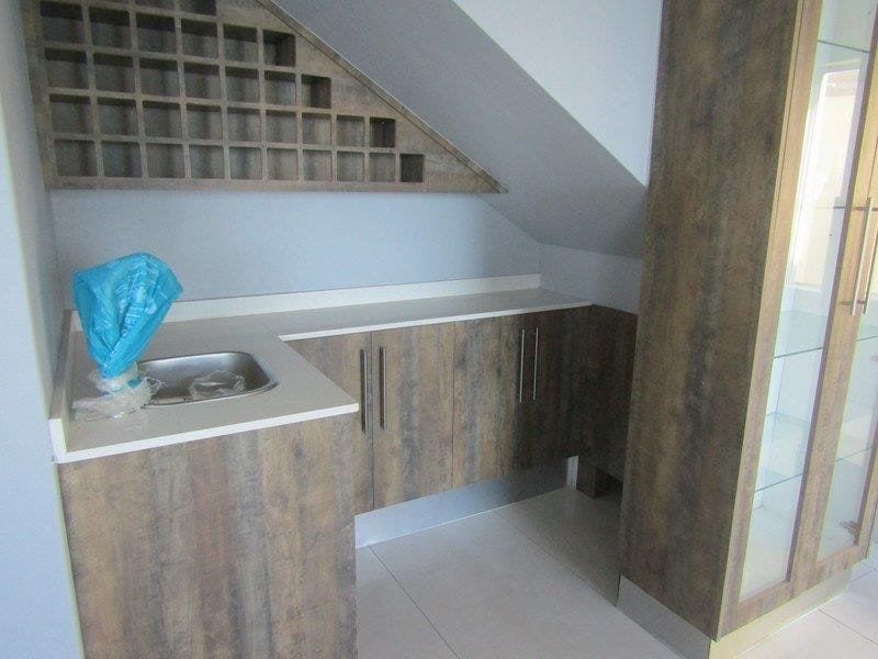 A compact scullery or bar area featuring wood-look built-in cabinetry, a sink, integrated wine storage, and a tall glass display cabinet.