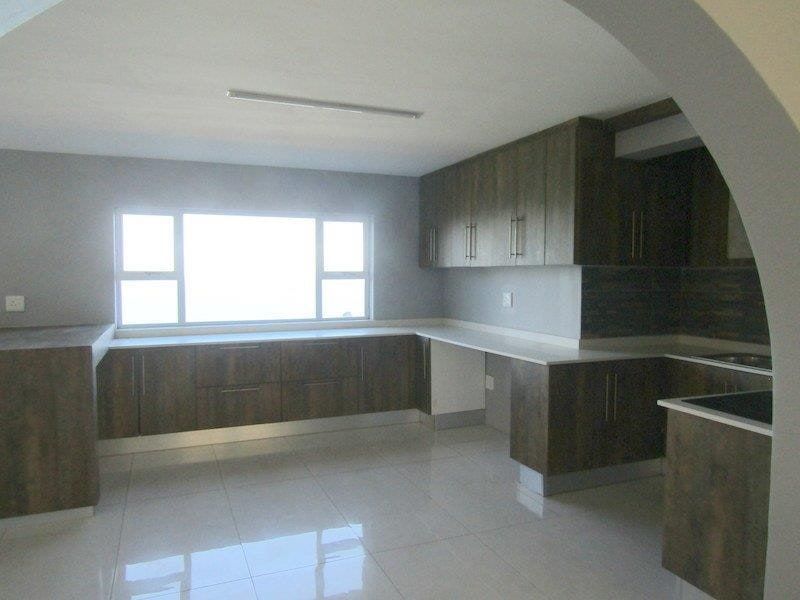 A spacious, modern kitchen featuring dark wood-finish cabinetry, light stone countertops, and neutral tiled flooring, viewed through a decorative architectural archway.