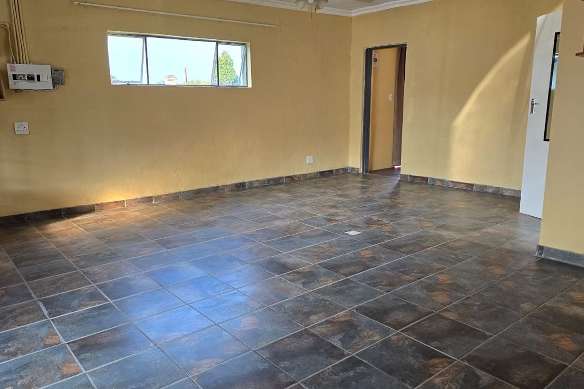 An empty living room featuring dark tiled flooring and yellow painted walls, providing a blank canvas for potential interior design updates.