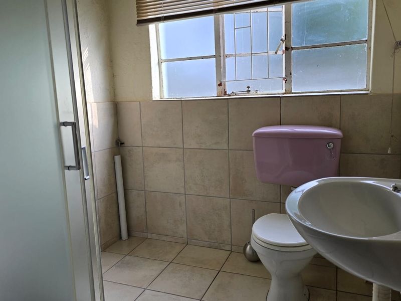 A functional bathroom featuring a pedestal basin, toilet, and shower enclosure with tiled finishes, requiring cosmetic updates to modernize the space.