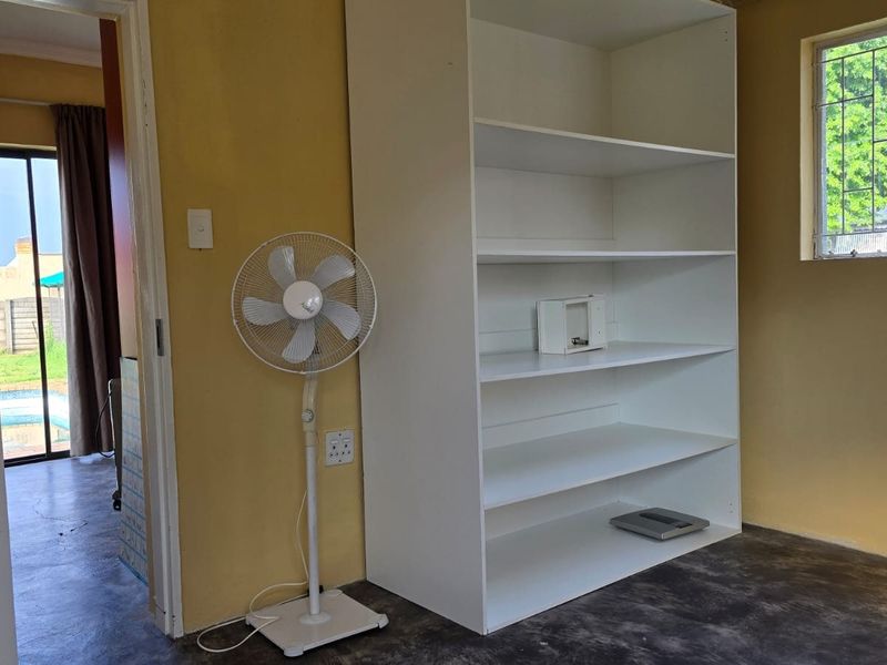 A simple bedroom featuring concrete flooring, a built-in white shelving unit, and a window with security bars.