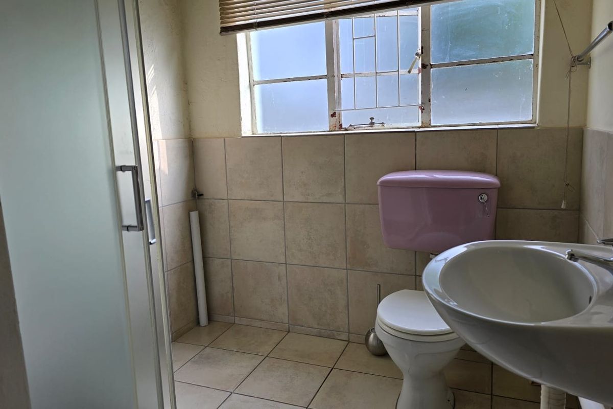 A functional bathroom featuring a pedestal basin, toilet, and shower enclosure with tiled finishes, requiring cosmetic updates to modernize the space.