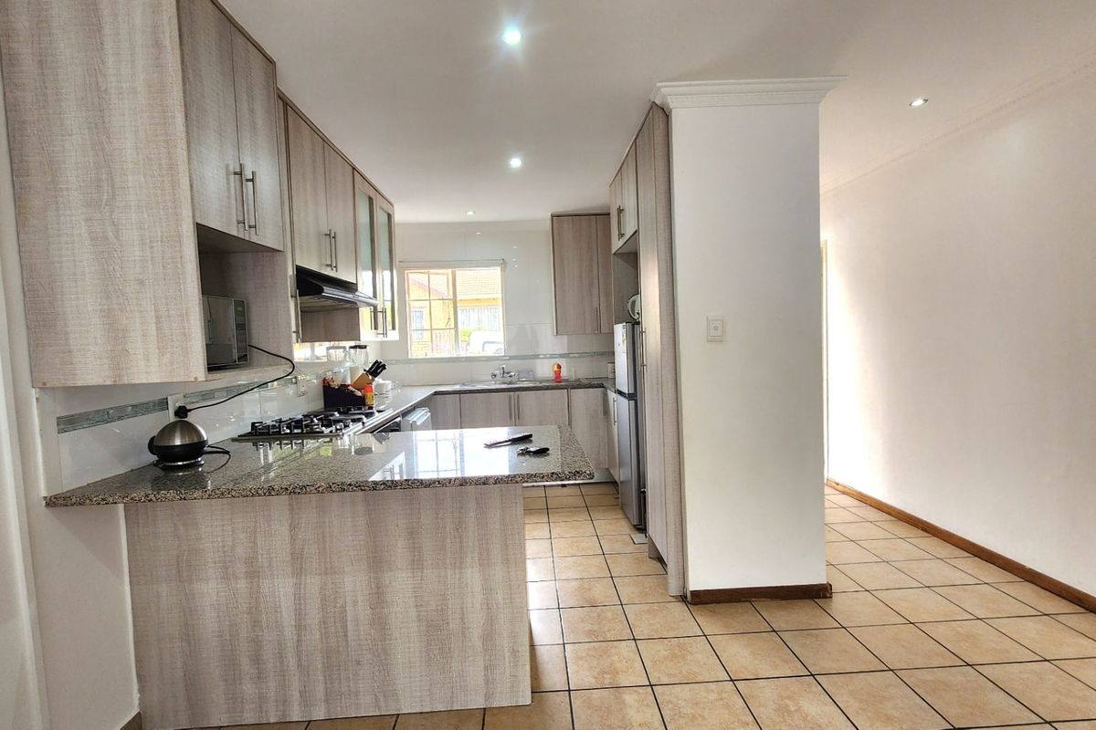 Modern kitchen featuring light wood-grain cabinetry, granite countertops, a gas hob with extractor fan, and tiled flooring throughout.