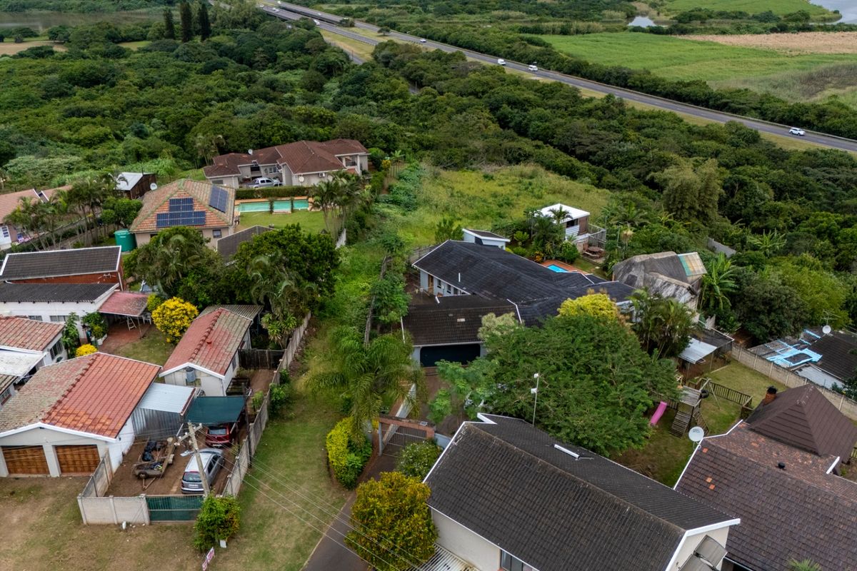 An aerial view of a residential neighborhood featuring multiple homes with tiled roofs, swimming pools, and established gardens near a main road.