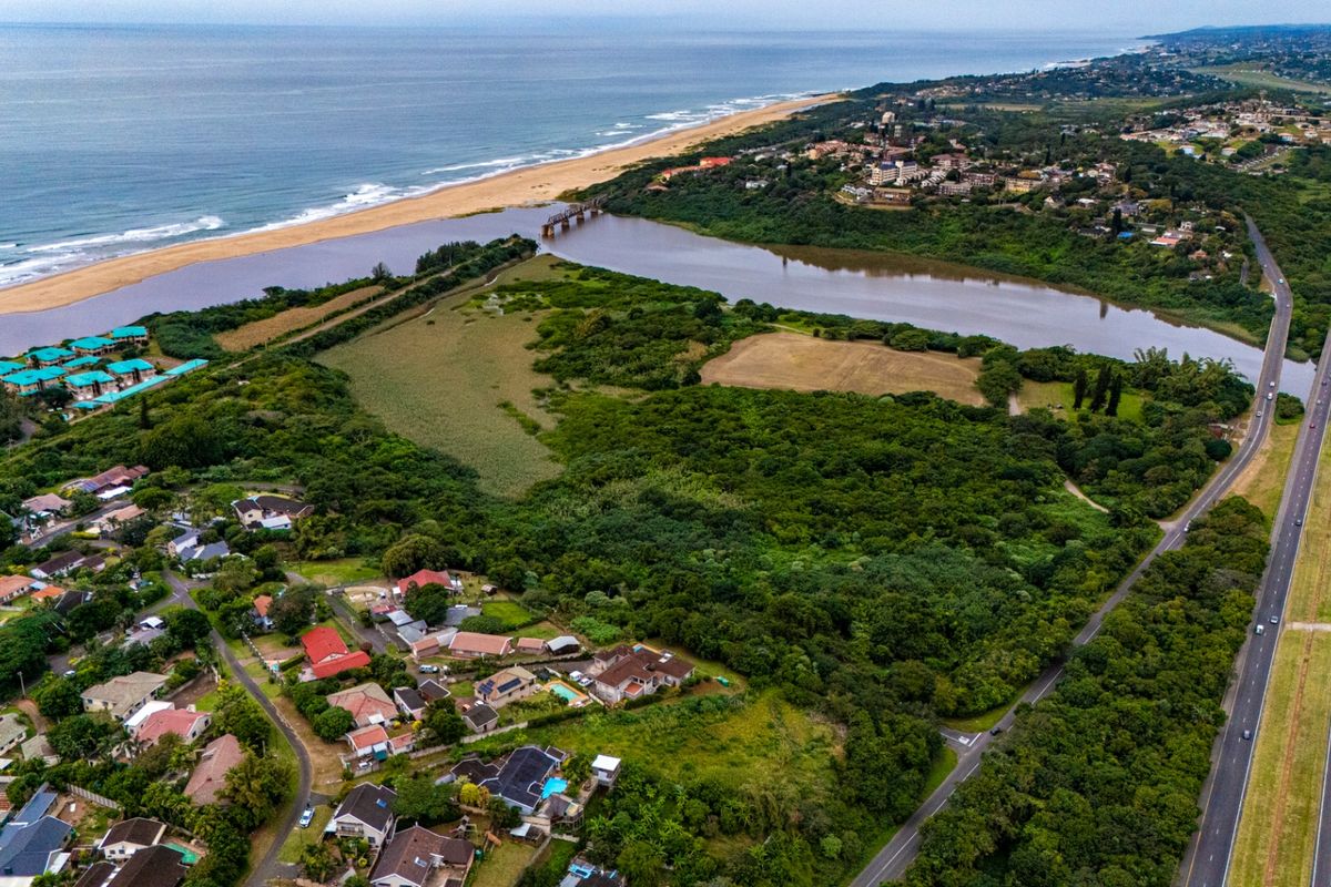 An aerial view of a coastal residential area featuring a river estuary, lush vegetation, and proximity to the ocean and major highway infrastructure.