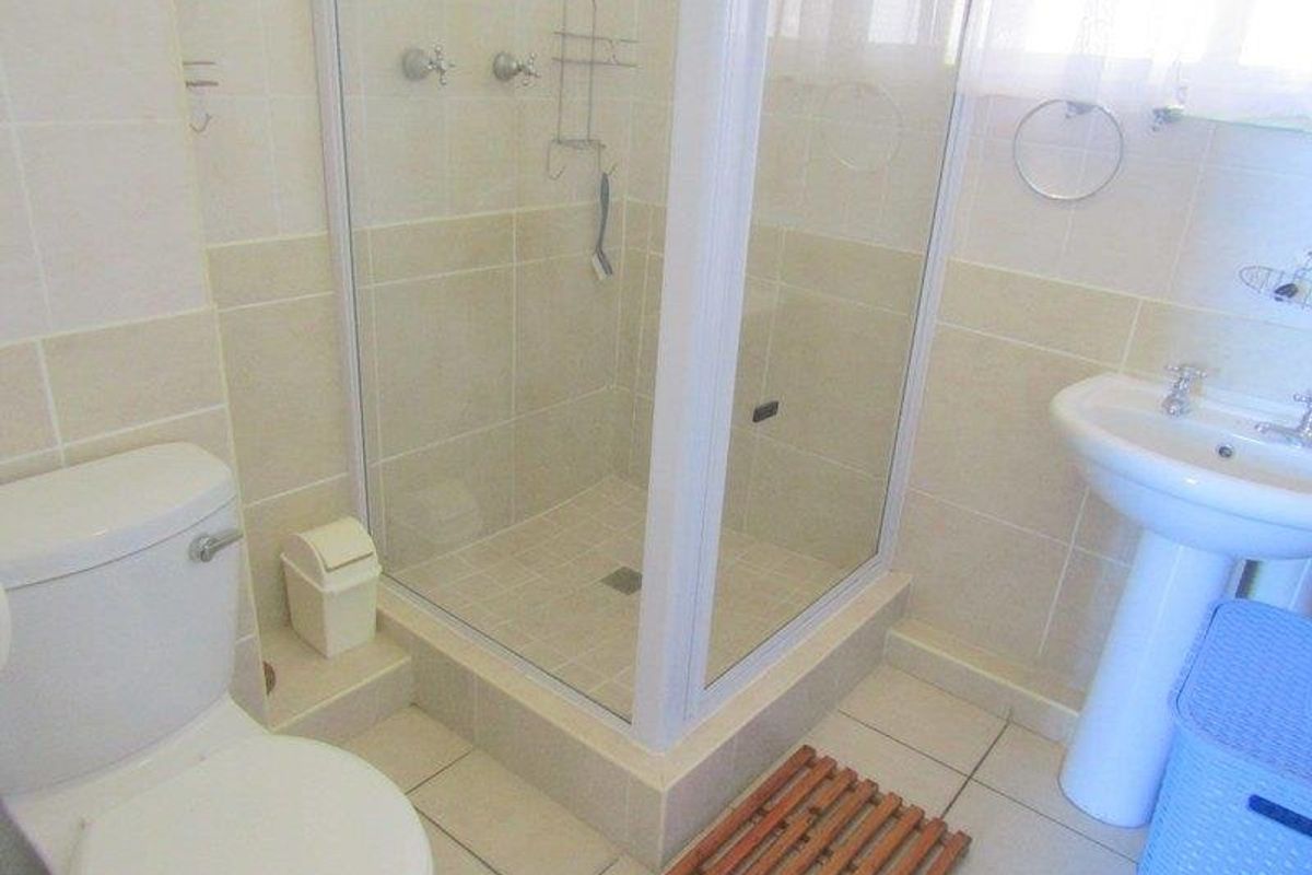 A functional bathroom featuring a glass-enclosed shower, pedestal basin, and toilet with neutral ceramic wall and floor tiling.