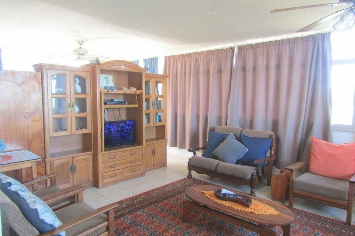 A living room area featuring tiled flooring and a ceiling fan, with large windows covered by curtains.