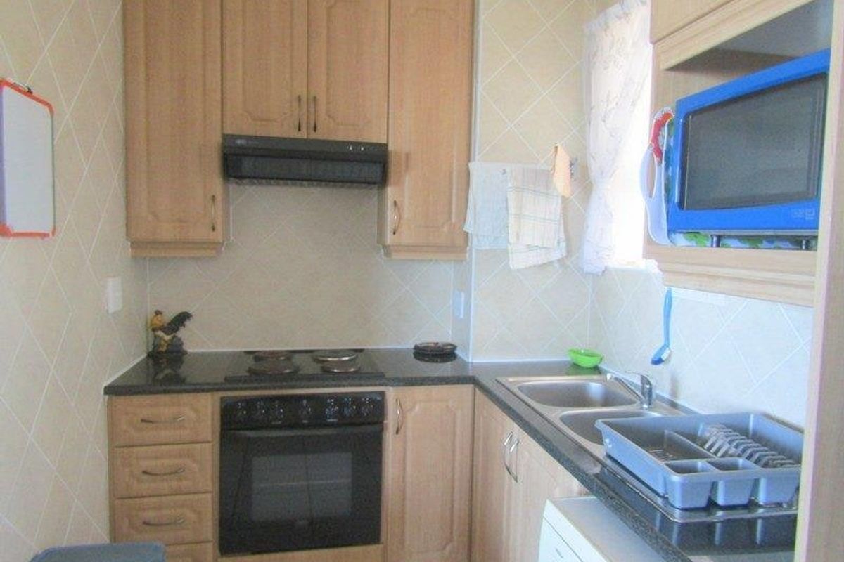 Compact kitchen featuring light wood cabinetry, granite countertops, a built-in oven with hob, and a double bowl stainless steel sink.