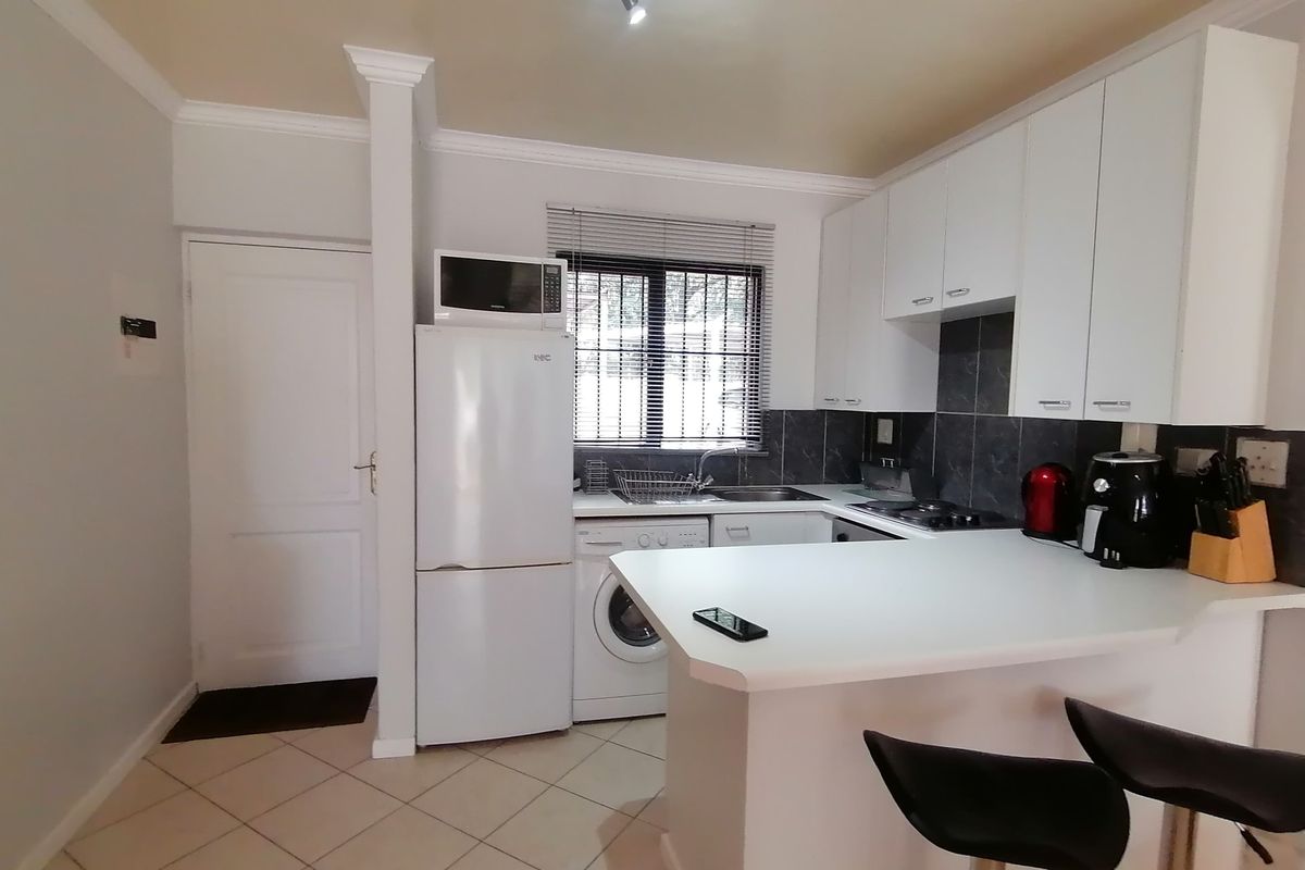 Compact kitchen featuring white cabinetry, a breakfast bar, tiled backsplash, and integrated laundry plumbing, offering a functional layout for an apartment.