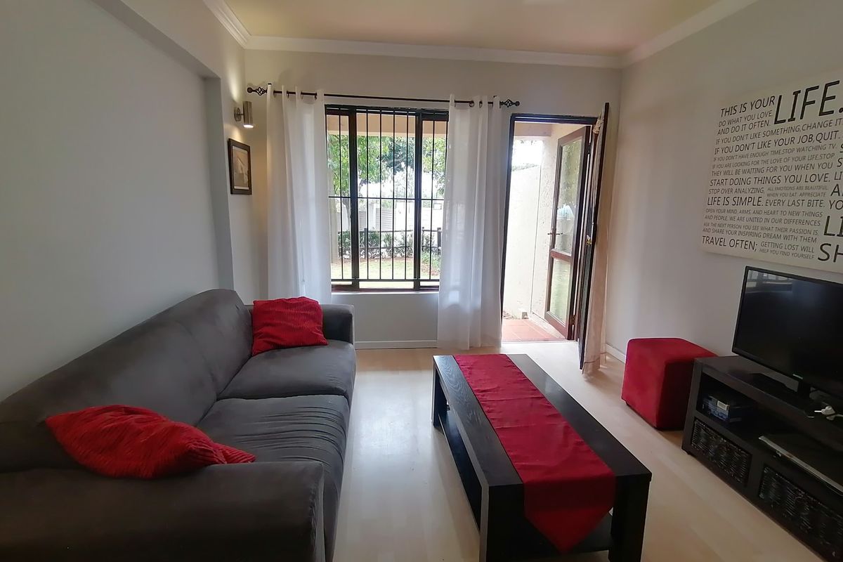 A comfortable living room featuring laminate flooring, cornicing, and direct access to an outdoor area through a glass door with security bars.