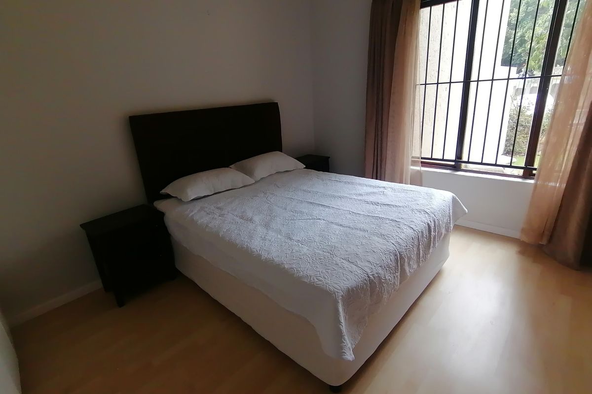 A bedroom featuring laminate flooring and a window fitted with security bars.