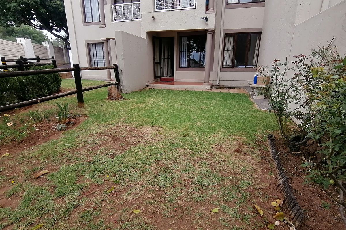A private rear garden area featuring a small paved patio, security-fitted entrance, and established lawn with timber fencing.
