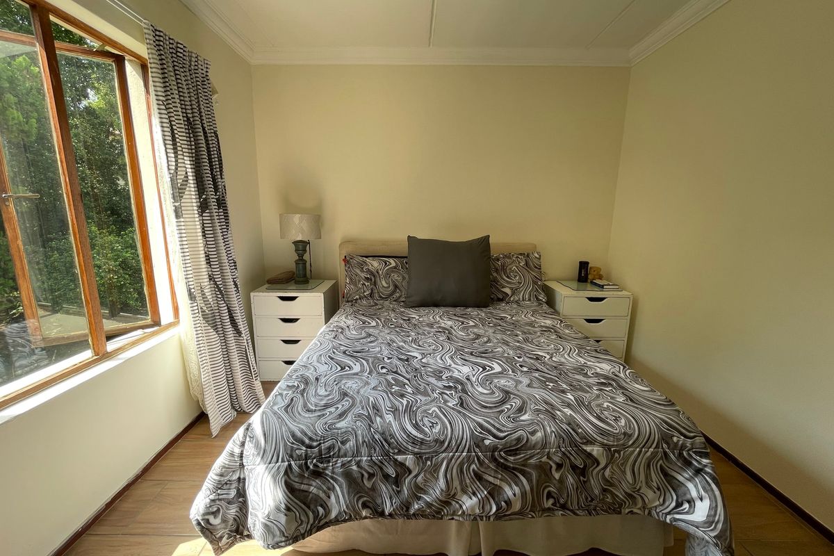 A well-lit bedroom featuring tiled flooring, a wooden window frame, and decorative ceiling cornicing.