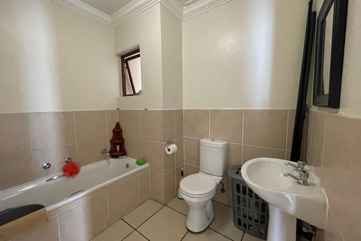 A functional bathroom featuring a bathtub, pedestal basin, and toilet with neutral wall and floor tiling.