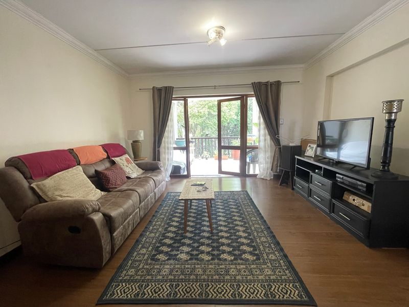 A living room featuring laminate flooring, crown molding, and direct access to an outdoor balcony through sliding glass doors.