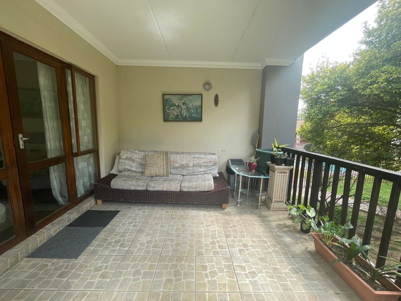 A covered patio area featuring tiled flooring, wooden framed glass sliding doors, and a protective railing overlooking the garden.